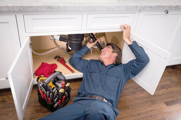 Plumber Under the sink looking at the pipes